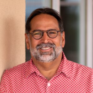 Man wearing red button-up shirt and glasses smiles to camera