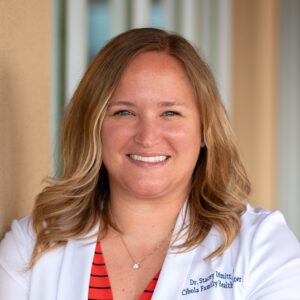 Blonde woman wearing red striped shirt and white lab coat smiles to camera